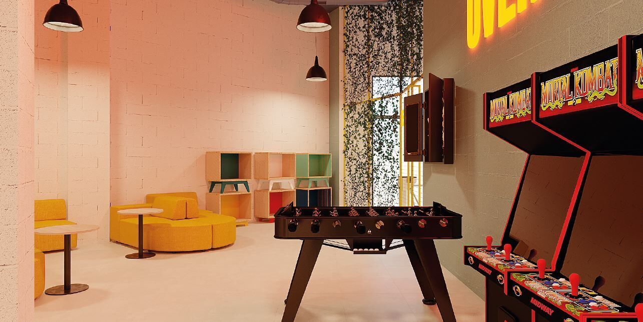 Una habitación con mesa de futbolín, sofás amarillos y letrero de neón.