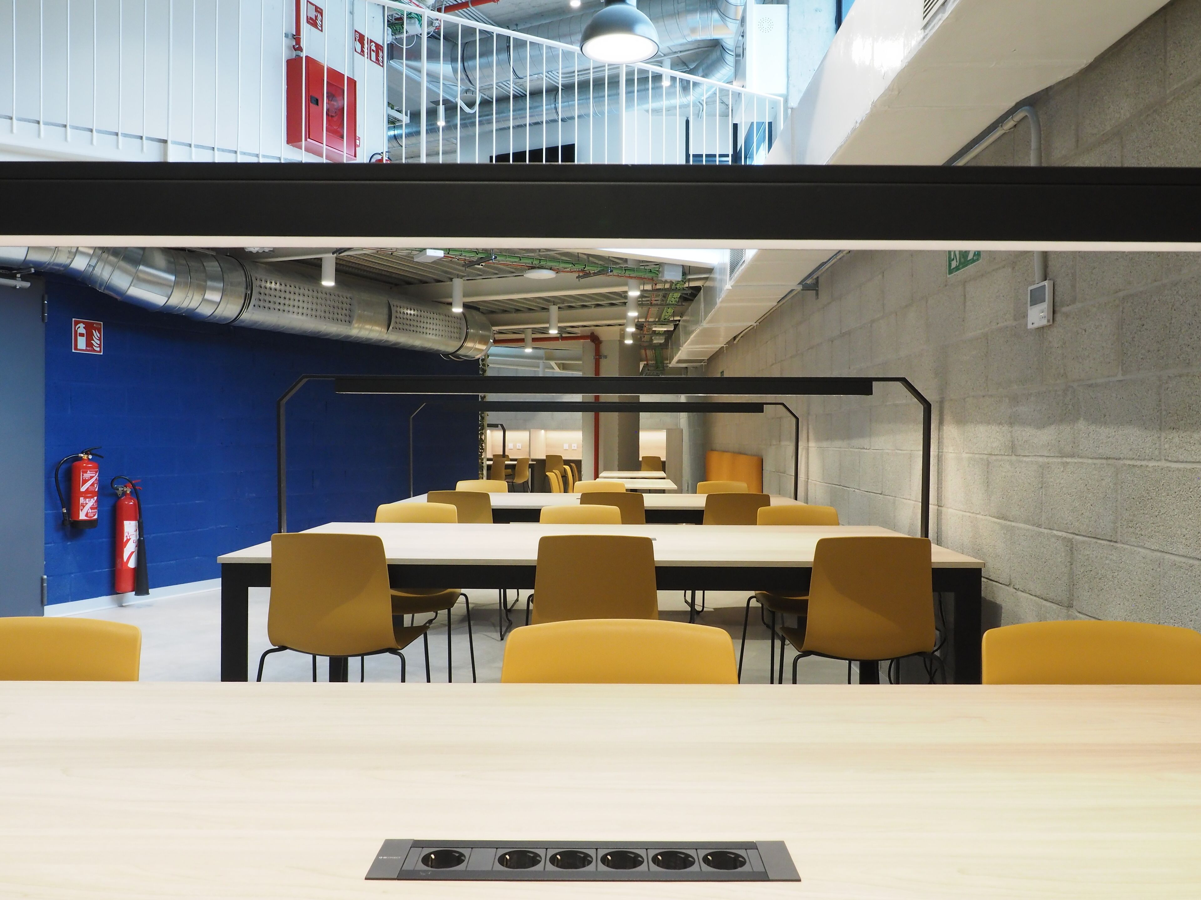 A conference room with tables and chairs, a fire extinguisher, and a visible ceiling with ductwork.