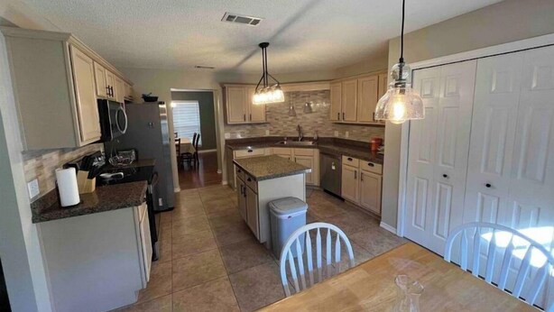 A spacious kitchen with granite countertops, white cabinets, and pendant lighting.