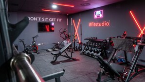 Un gimnasio con equipamiento de ejercicio, un televisor montado en la pared y letreros de neón motivacionales.