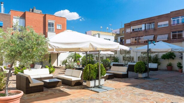 Un patio al aire libre con mobiliario de mimbre, sombrillas blancas y plantas en macetas.