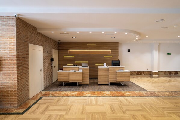 A reception area with a brick wall, wooden reception desk, and a herringbone patterned floor. - Micampus Leganés (Leganes)