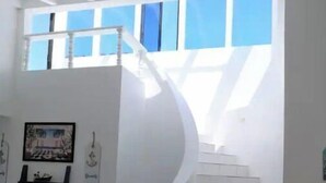 A spiral staircase in a modern interior with white walls and a view of the sky through large windows. - Mi Sueño Casita 2 - Directly on sandy beach (Ensenada)