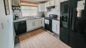 A compact kitchen with white cabinets, a black refrigerator, a stove, and a dishwasher. - 3 Bedroom Modern Vintage in Historic Sanford (Sanford)
