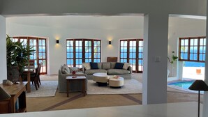 Ein geräumiges Wohnzimmer mit großem Fenster und Meerblick, einer Sofagarnitur, einem Esstisch und einem Couchtisch.