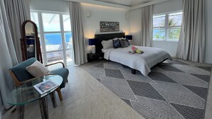 Ein modernes Hotelzimmer mit einem großen Bett, einer Sitzecke mit Glastisch und Blick auf den Ozean.