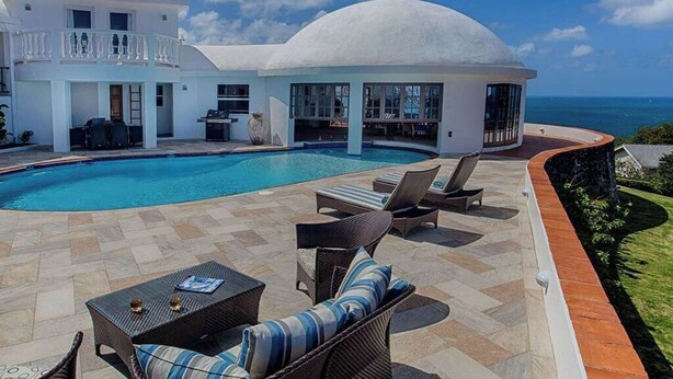 Eine luxuriöse Villa mit Swimmingpool, Sitzgelegenheiten im Freien und Blick aufs Meer.