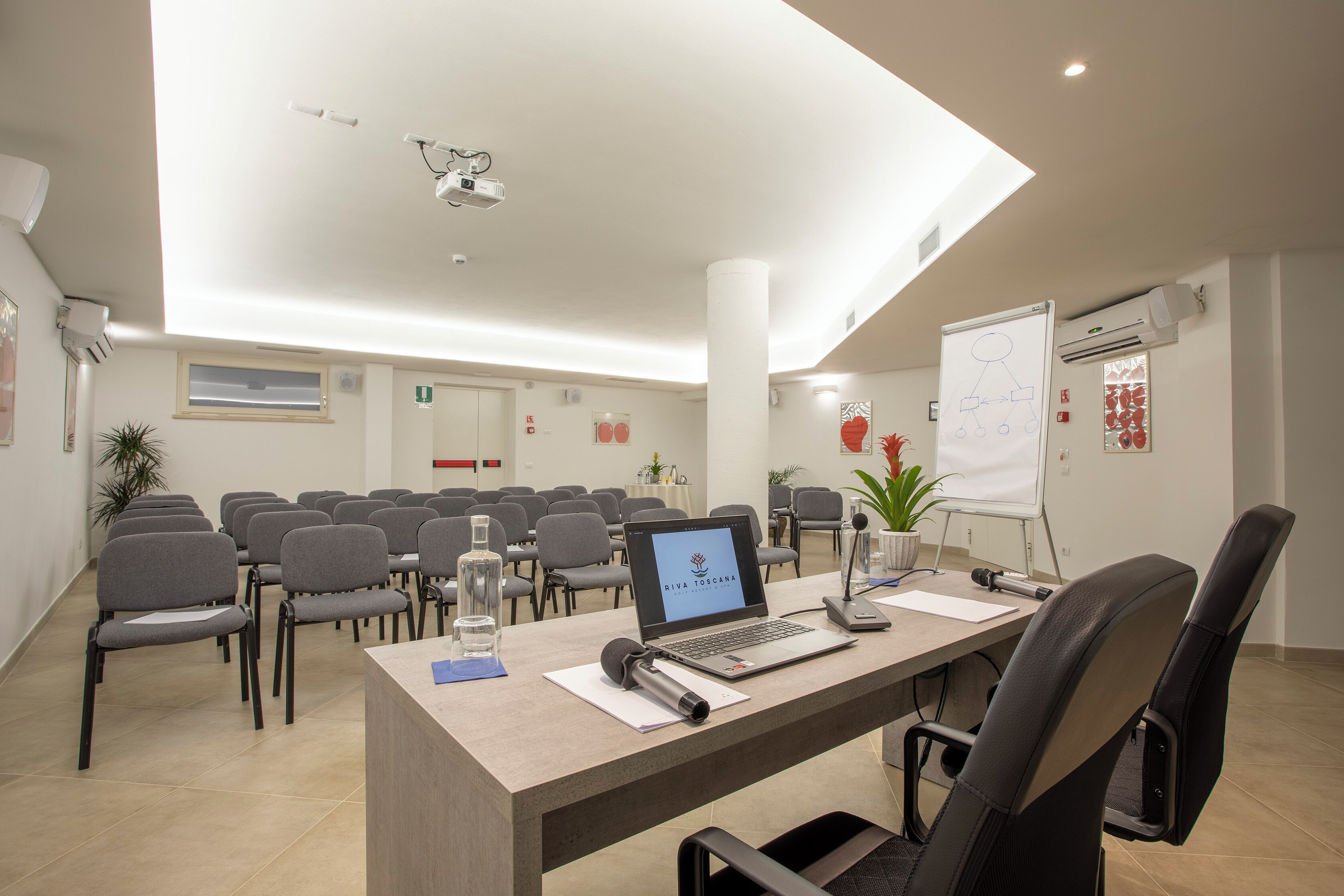 Una sala de conferències amb una taula llarga, cadires, un ordinador portàtil, una pissarra i un projecte.