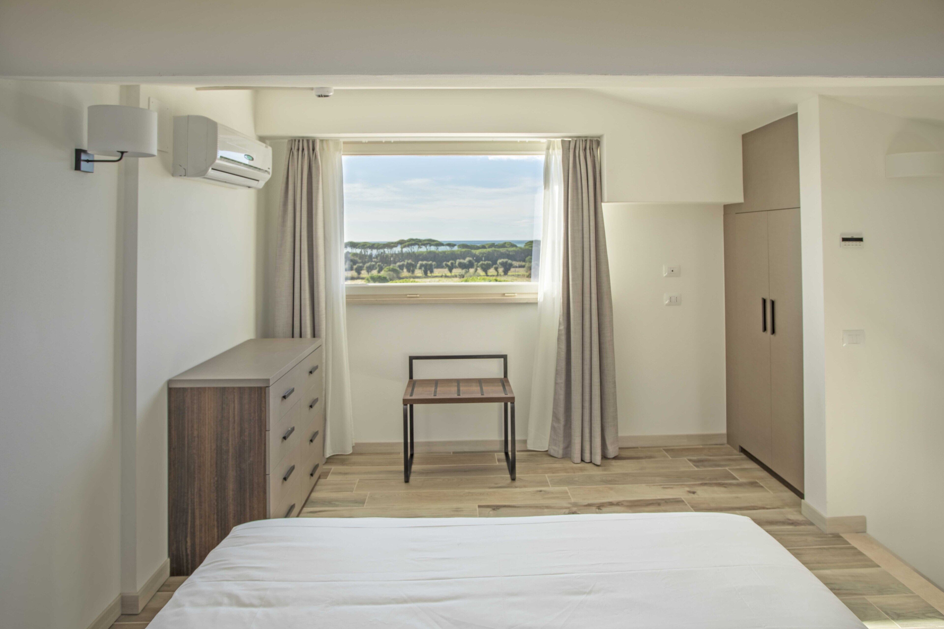 A bedroom with a bed, a desk, a wardrobe, and a window with curtains.