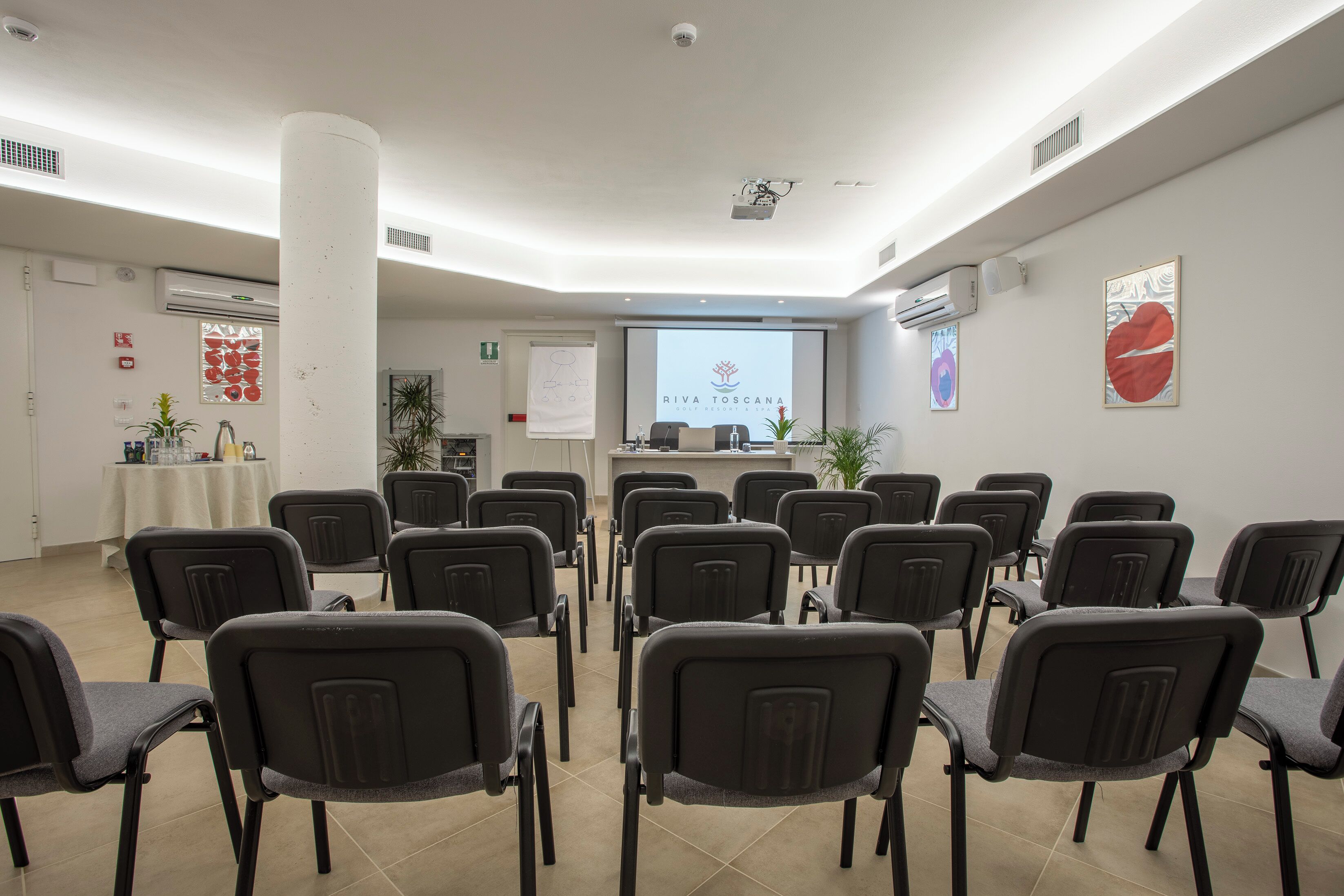 Un salón de conferencias con filas de sillas, un atril y una pantalla proyectora que muestra 