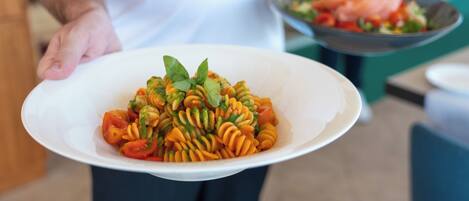 A person holding a white bowl with a pasta dish garnished with basil.