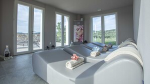A spa room with a large window, a massage table, and a wall-mounted massage machine. - Riva Toscana Golf Resort & SPA (Follonica)