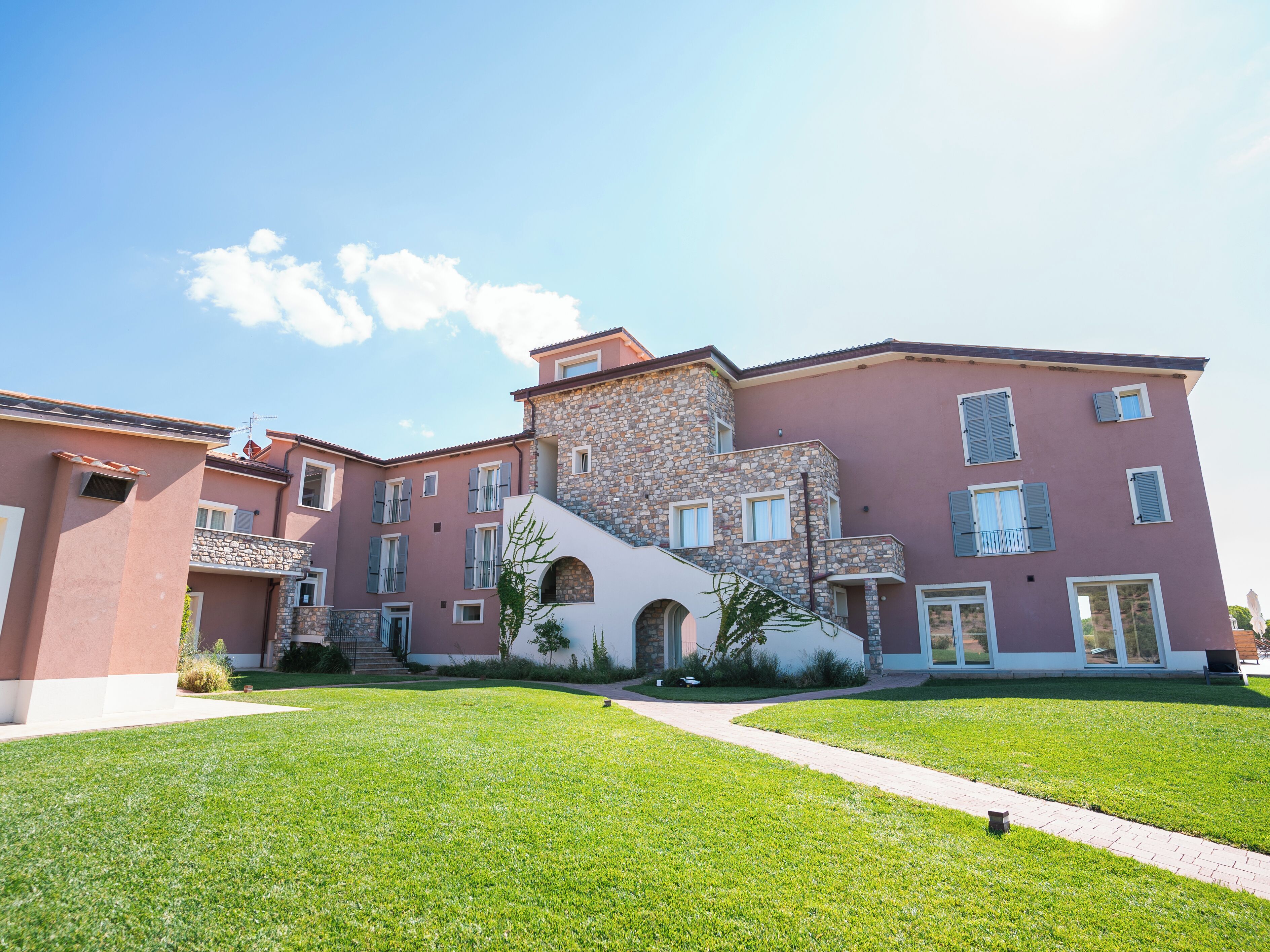 A multi-story building with a stone facade, a central arched entrance, and a well-maintained lawn.