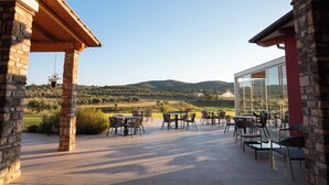An outdoor patio with stone pillars, tables, and chairs, overlooking a scenic landscape with hills and a clear sky. - Riva Toscana Golf Resort & SPA (Follonica)
