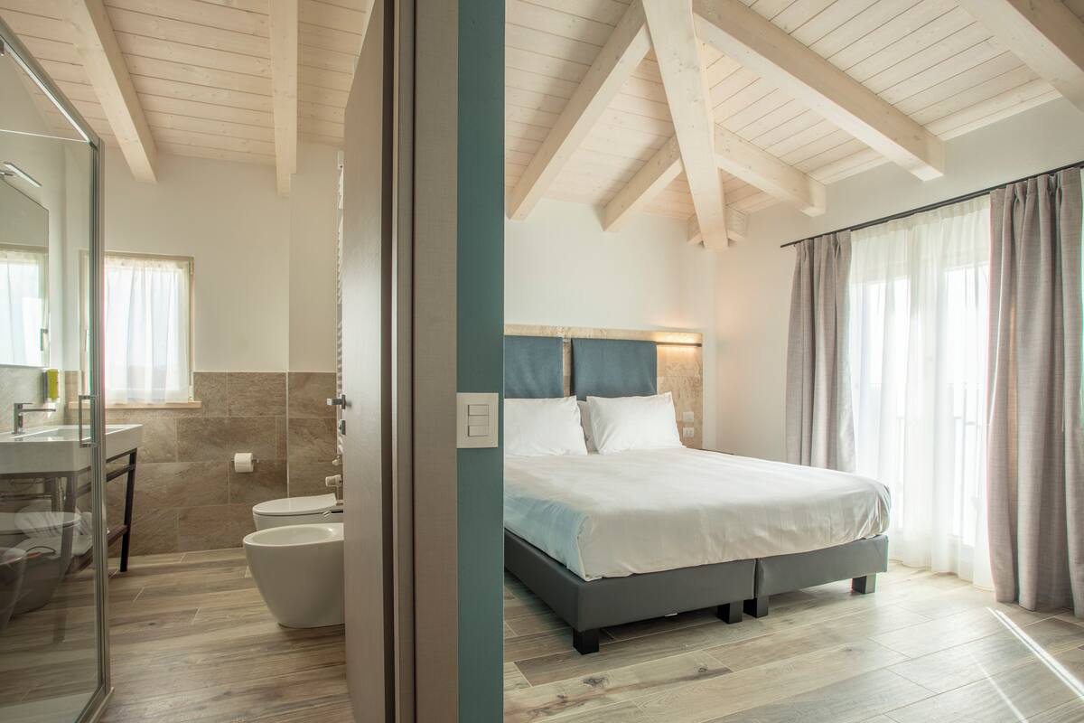 A modern bedroom with a large bed, a bathroom with a bathtub, and a glass shower enclosure.