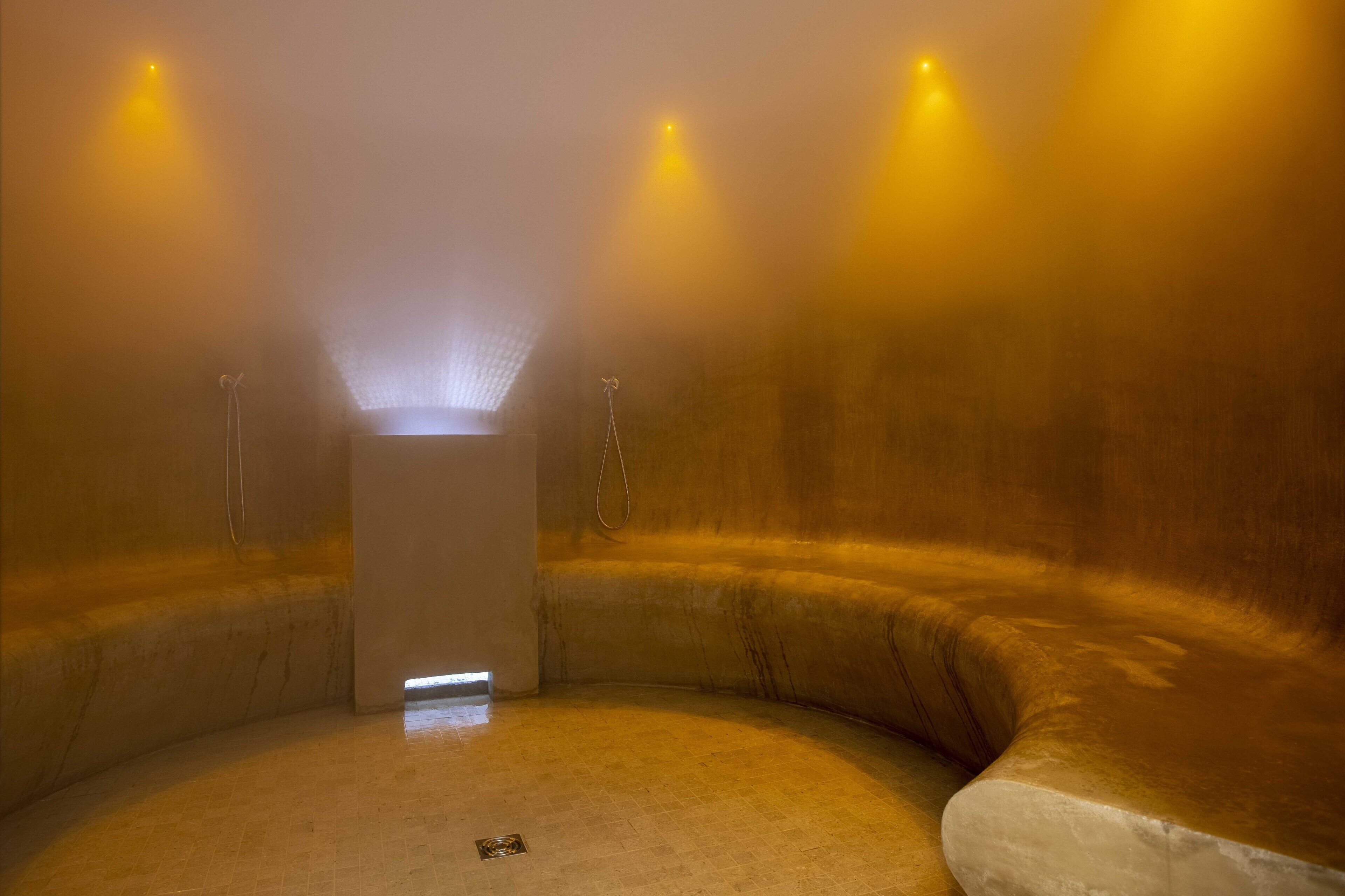 A steam room with a central pillar, curved walls, and three ceiling lights.