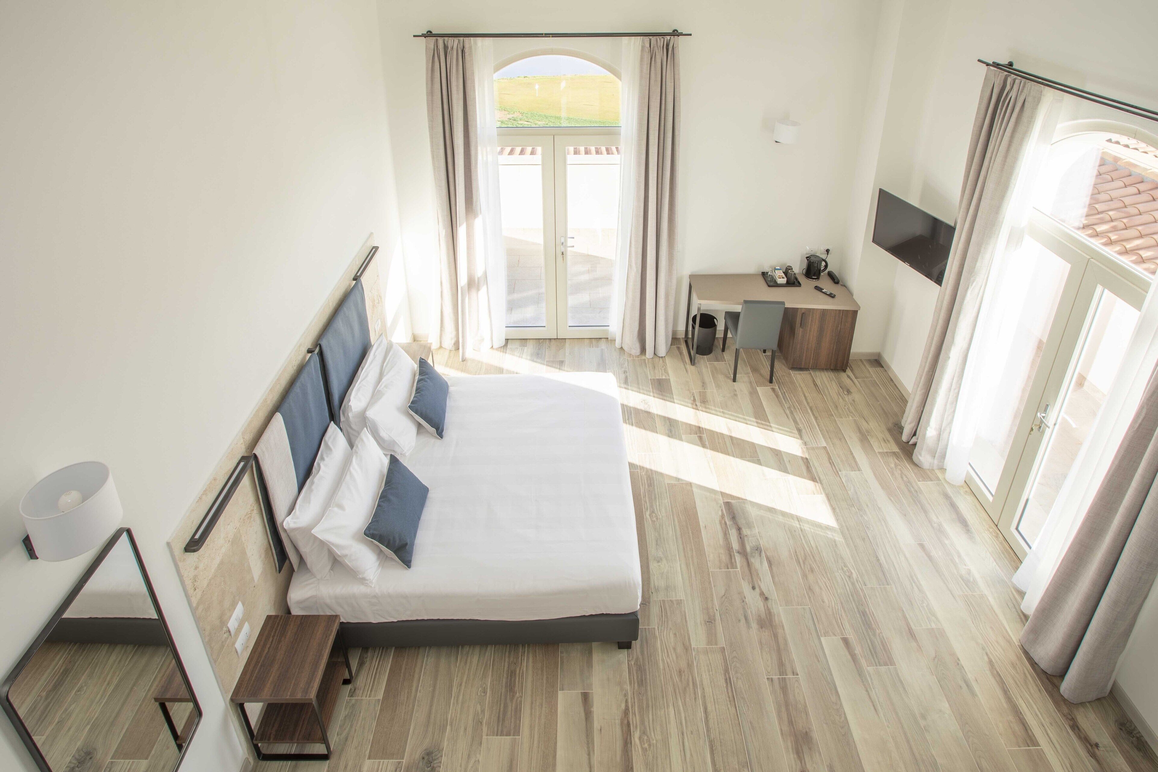 Ein Schlafzimmer mit einem großen Bett, einem Schreibtisch und Blick ins Freie durch eine Schiebetür.