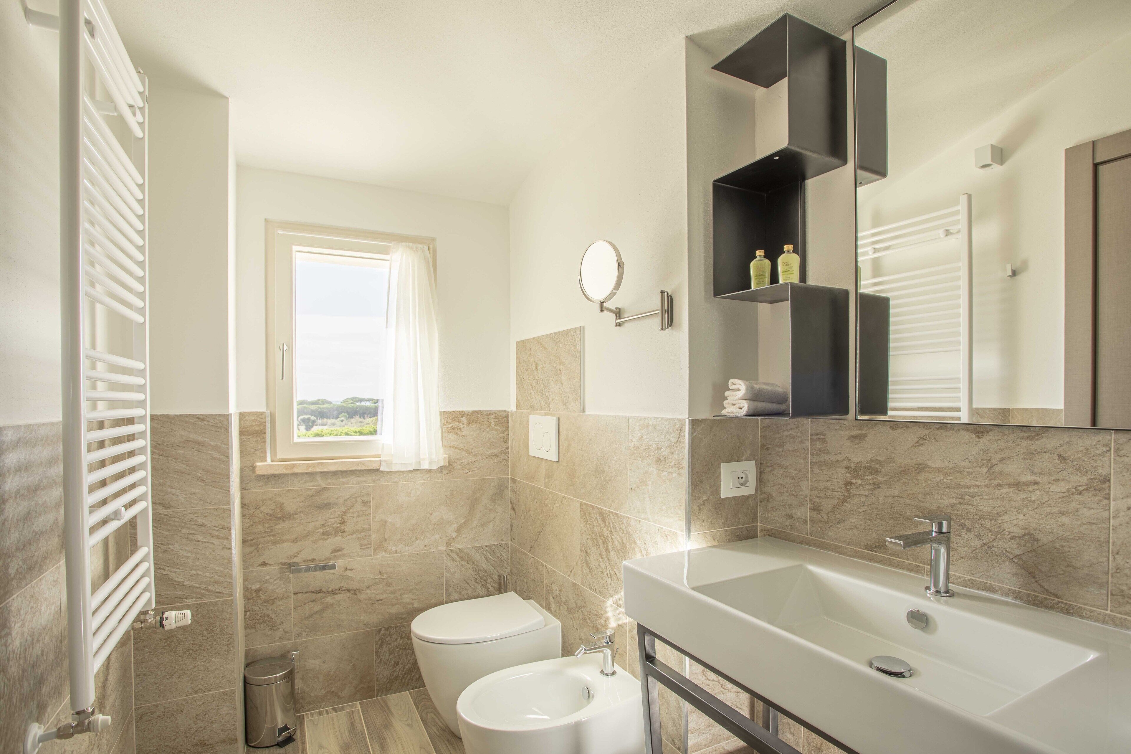 A modern bathroom with a large sink, toilet, and a window providing a view of the outdoors.