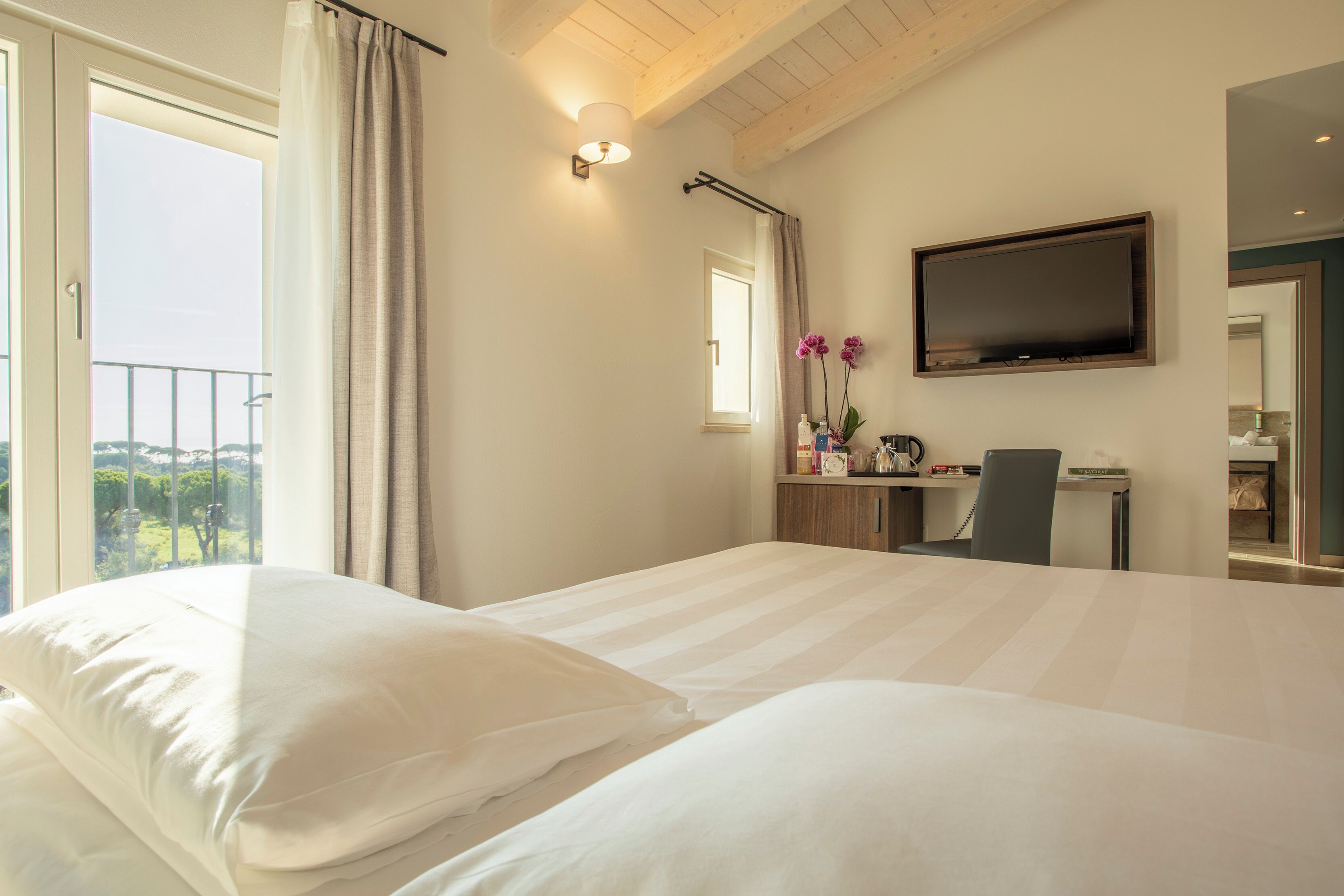 A hotel room with a large bed, a desk with a chair, a flat-screen TV, and a window with curtains.