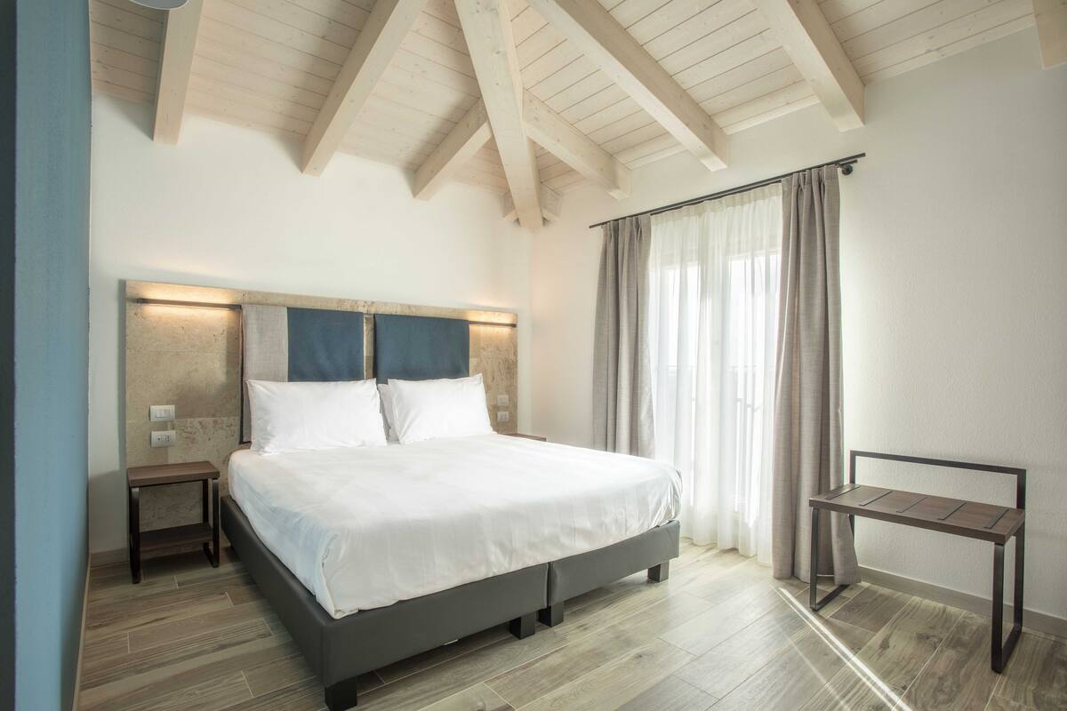 A bedroom with a bed, bedside tables, a desk, and a window with curtains.