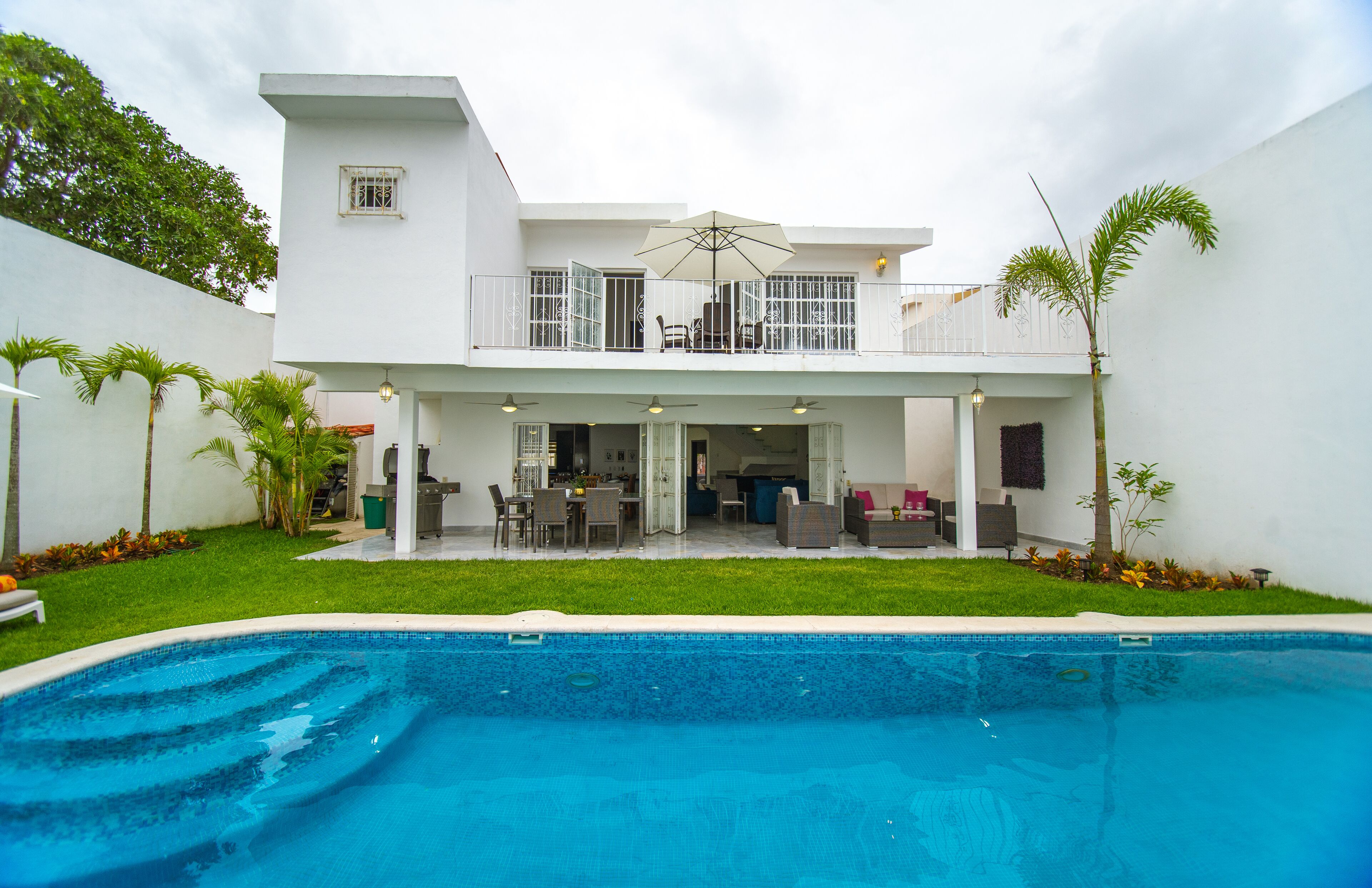 A two-story house with a balcony, a swimming pool, and a patio area with outdoor furniture.