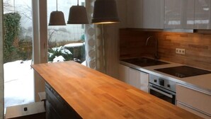 Une cuisine moderne dotée d’un plan de travail en bois, d’appareils électroménagers en acier inoxydable et de luminaires suspendus.
