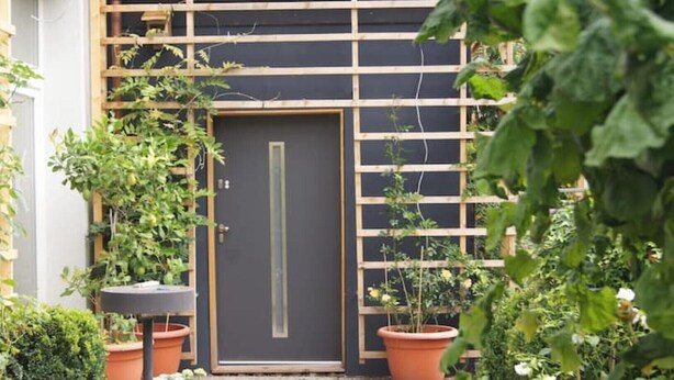 Un jardin agrémenté d’une treille en bois, de plantes en pot et d’une porte.