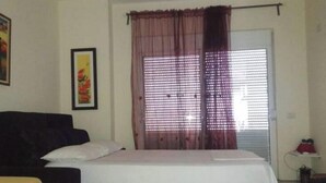 A bedroom with a bed, a couch, a small table, and a window with curtains.