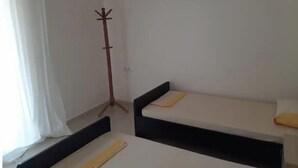 A small, simple room with two single beds, a coat rack, and a window with curtains. - Family apartment 5 by Hillside apartments TM (Sarande)