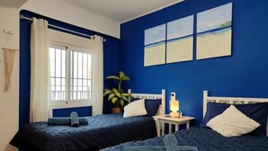 Una habitación con dos camas, una ventana con cortinas, una lámpara de noche y una planta.