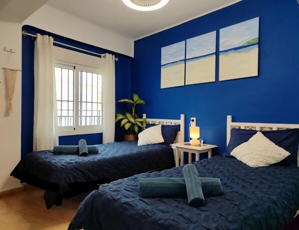Une chambre avec deux lits, une fenêtre avec des rideaux, une lampe de chevet et une plante.