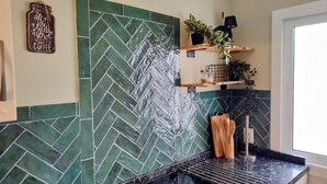 Una cocina con salpicadero de baldosas tipo espiga, estanterías de madera con plantas y encimera negra.