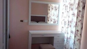 Quarto com parede rosa, penteadeira branca com gavetas, espelho e cortina florida.