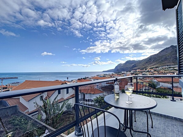 A balcony with a table and chairs, overlooking a coastal town and the sea. - Casa da Av by Atlantic Holiday (Machico)
