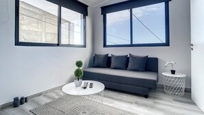 Een moderne woonkamer met een grijze bank, een ronde salontafel en een bijzettafeltje met een plant in een pot.