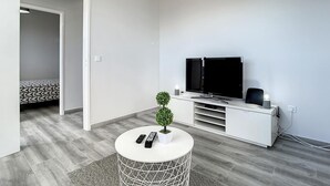 Een moderne woonkamer met een flatscreen televisie, een klein rond tafeltje met een plant en een witte tv-meubel.