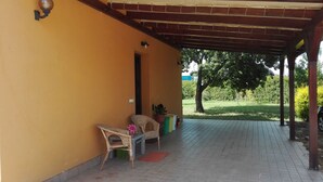 A covered patio area with two wicker chairs and a small table, a potted plant, and a tiled floor.