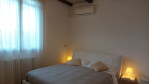A bedroom with a bed, bedside lamps, a radiator, and an air conditioning unit.