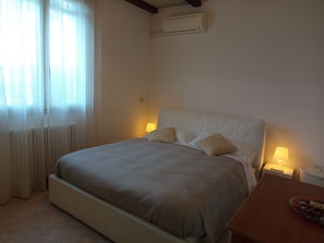 Quarto com cama, luminárias de cabeceira, radiador e aparelho de ar condicionado.