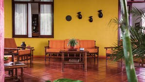 A room with a yellow wall, a wooden sofa, a coffee table, and a window with curtains.