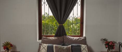 Un dormitorio con una cama, una ventana con cortinas, una mesita de noche con una lámpara y un jarrón con flores.