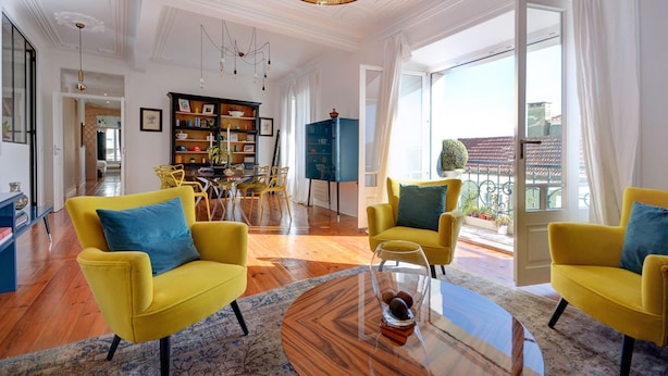 Un salón amplio con sillones amarillos, una mesa de centro de vidrio y una lámpara de araña moderna.