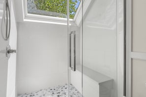Une douche avec une porte en verre, des murs recouverts de carreaux blancs et un puits de lumière.