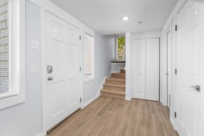 A hallway with white doors, a staircase, and a window with blinds.