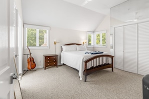 A bedroom with a bed, a guitar, a nightstand, a dresser, and a closet.