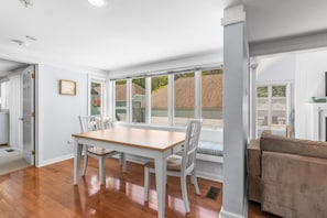 A dining area with a wooden table and chairs, a window with a view of a wooden deck, and a beige sofa.