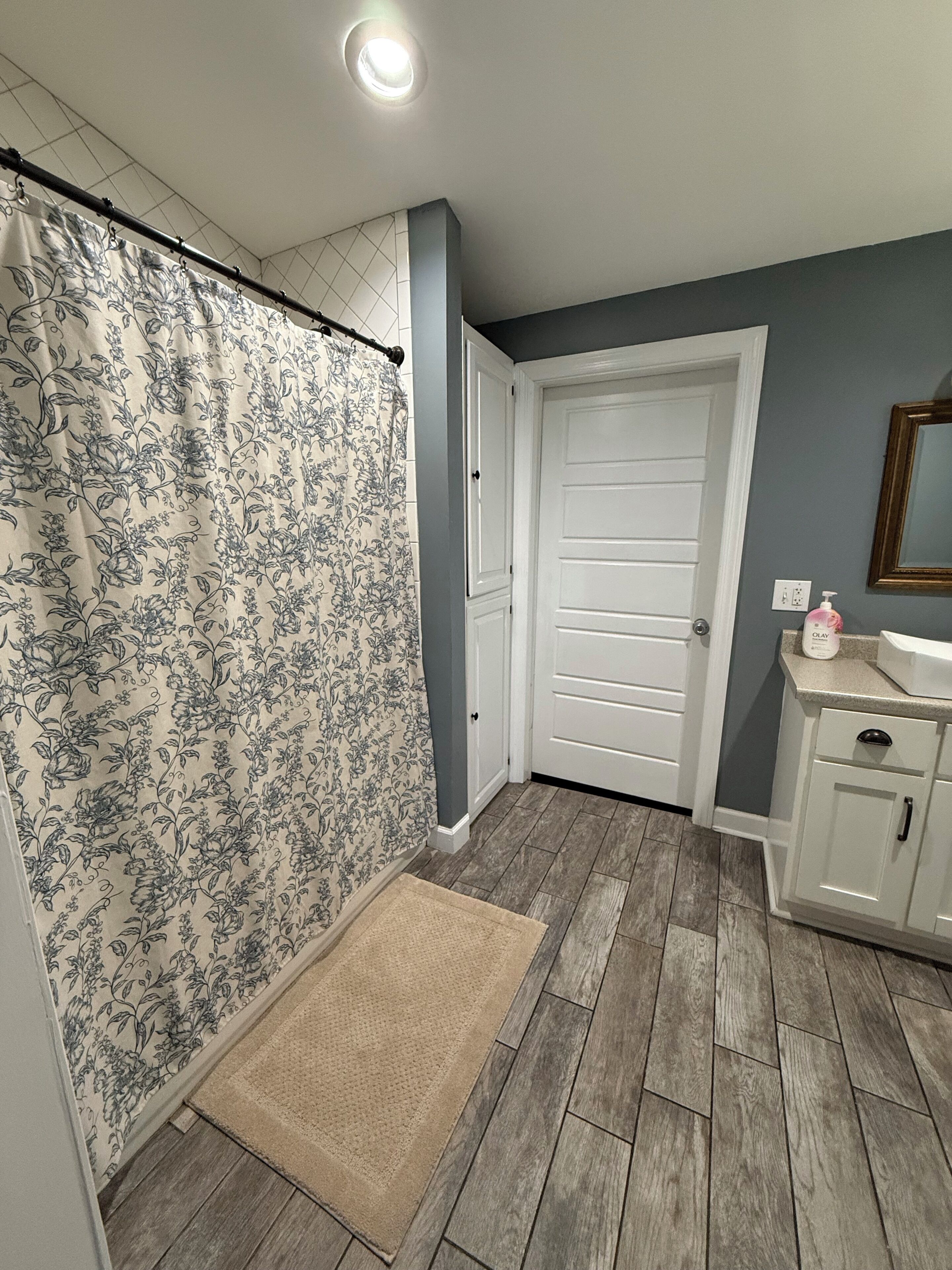 A bathroom with a shower curtain, a door, a sink with toiletries, and a mirror.