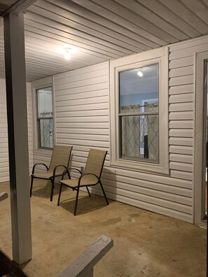 A covered porch with two chairs and a window.