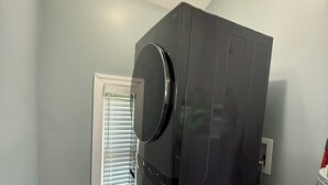 Quarto compacto com máquina de lavar e secar integradas, piso de madeira e janela com persianas.