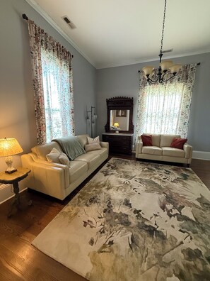 A living room with two sofas, a large rug, a chandelier, and a mirror.